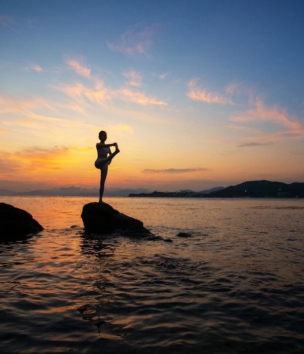 Silhouette of a person in a powerful yoga warrior pose against a sunrise.